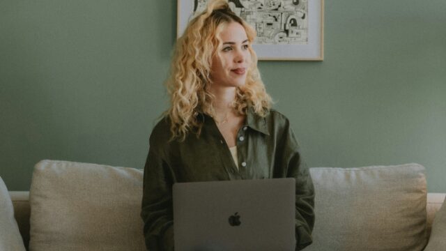a young woman sits on a sofa with her laptop